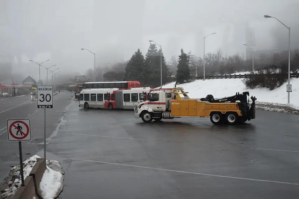 Sisli bir günde körüklü bir otobüsü çeken sarı ağır kurtarma aracı