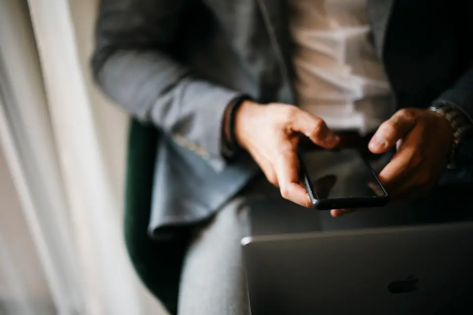 Dizüstü bilgisayarın başında akıllı telefon kullanan eller